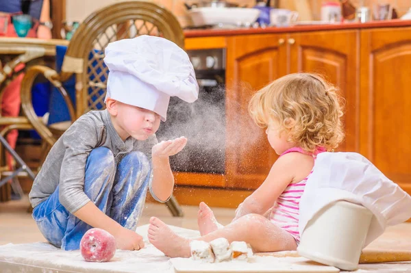 Dos hermanos - niño y niña - en sombreros de chef sentados en el kitc — Foto de Stock