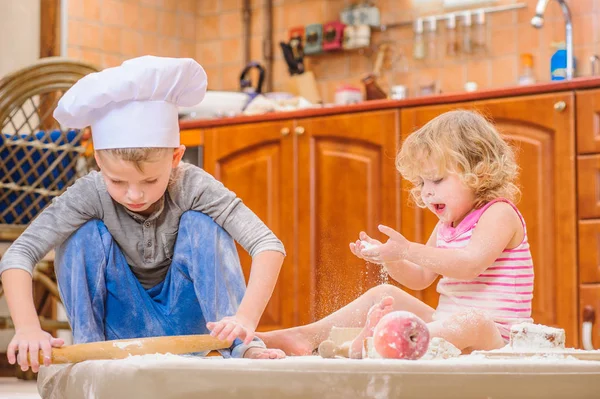 Zwei Geschwister - Junge und Mädchen - in Kochmützen auf dem Kitsch sitzend — Stockfoto