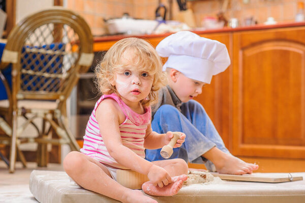 Two siblings - boy and girl - in chef's hats sitting on the kitc
