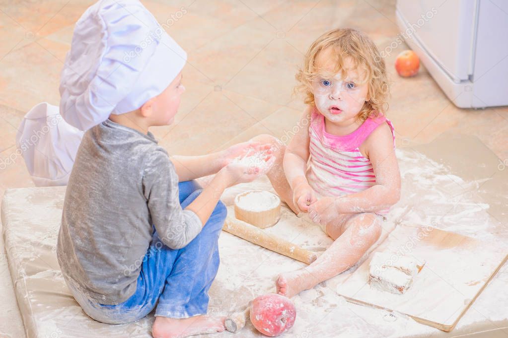Two siblings - boy and girl - in chef's hats sitting on the kitc