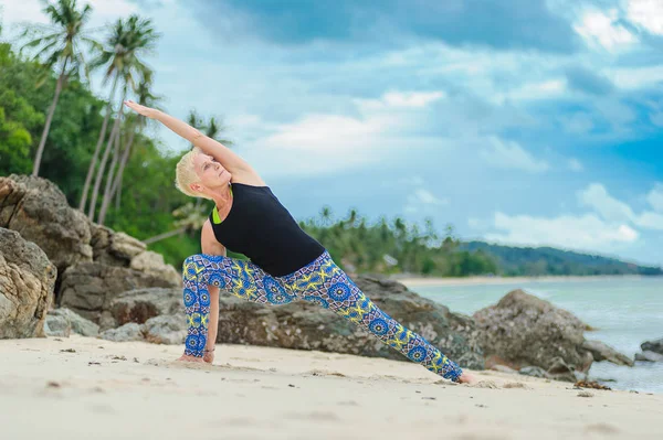 Güzel olgun yaşlı kadın bir ıssız tropikal beac Yoga yapıyor