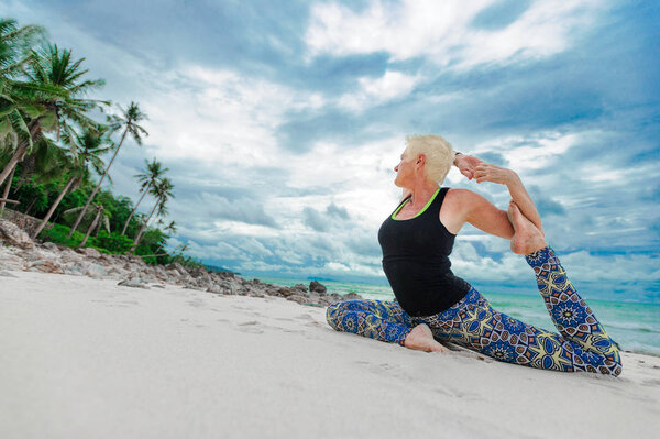 Beautiful mature aged woman doing yoga on a desert tropical beac