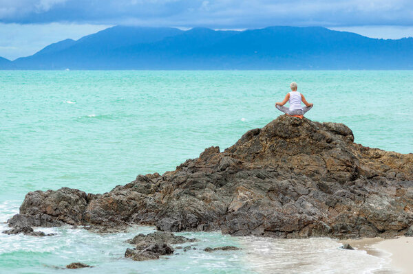 Beautiful mature aged woman sits on top of a cliff doing yoga