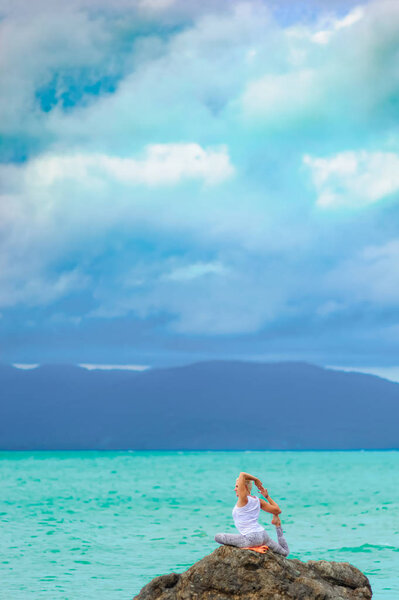 Beautiful mature aged woman sits on top of a cliff doing yoga