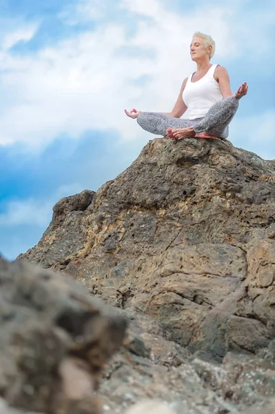 Güzel Olgun kadın oturur yoga yaparken bir uçurumun üstünde yaşlı