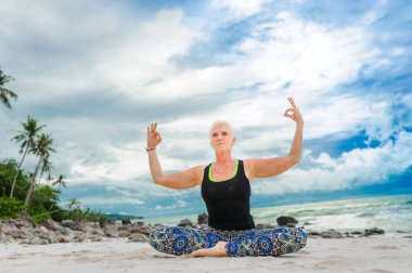 Güzel olgun yaşlı kadın bir ıssız tropikal beac Yoga yapıyor