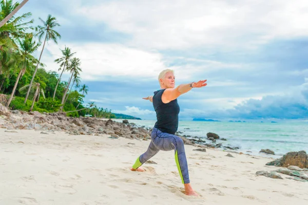 Güzel olgun yaşlı kadın bir ıssız tropikal beac Yoga yapıyor