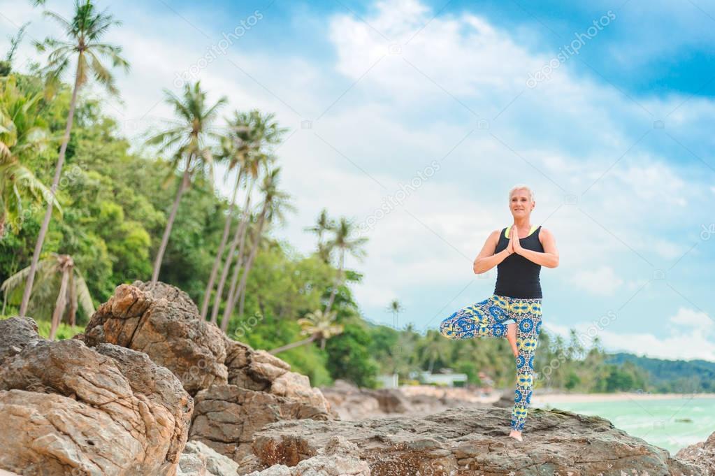 Beautiful mature aged woman doing yoga on a desert tropical beac