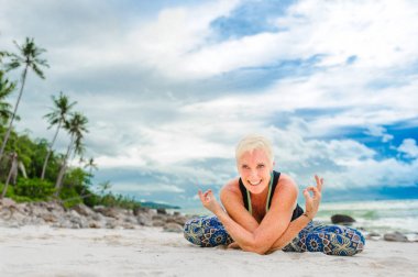 Güzel olgun yaşlı kadın bir ıssız tropikal beac Yoga yapıyor
