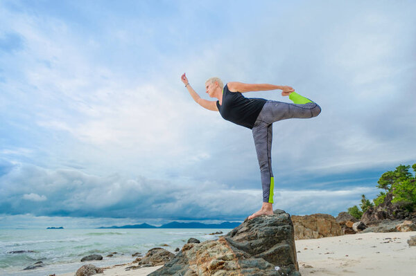 Beautiful mature aged woman doing yoga on a desert tropical beac