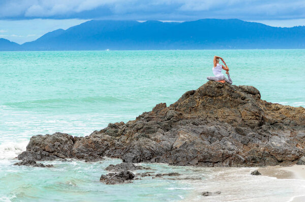 Beautiful mature aged woman sits on top of a cliff doing yoga