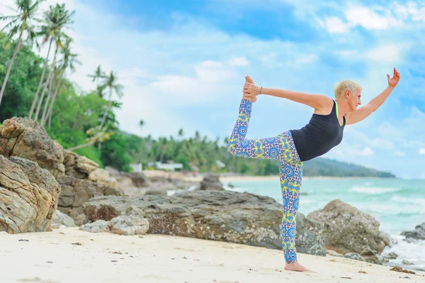 Güzel olgun yaşlı kadın bir ıssız tropikal beac Yoga yapıyor