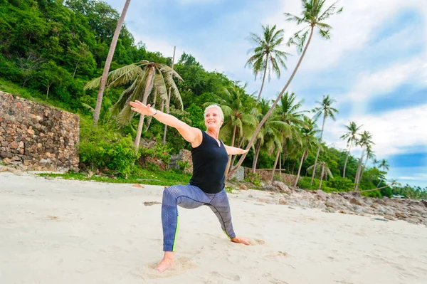 Beautiful mature aged woman doing yoga on a desert tropical beac — Stock Photo, Image