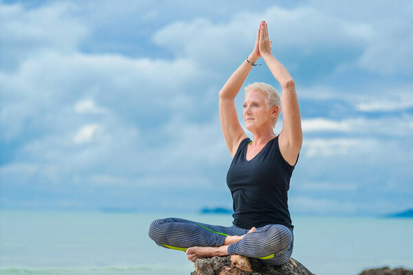 Beautiful mature aged woman doing yoga on a desert tropical beach