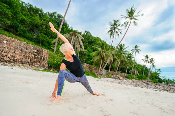Güzel olgun yaşlı kadın bir ıssız tropikal beac Yoga yapıyor