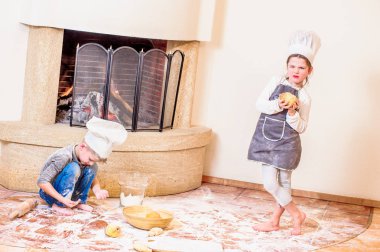 İki kardeş, erkek ve kız, şöminenin yanında şef şapkası takıyorlar. 