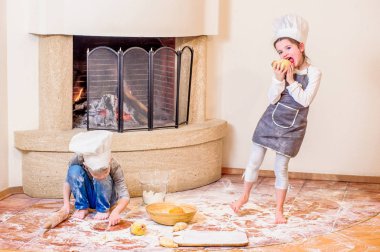 İki kardeş, erkek ve kız, şöminenin yanında şef şapkası takıyorlar. 