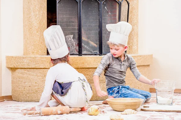 İki kardeş, erkek ve kız, şöminenin yanında şef şapkası takıyorlar. 