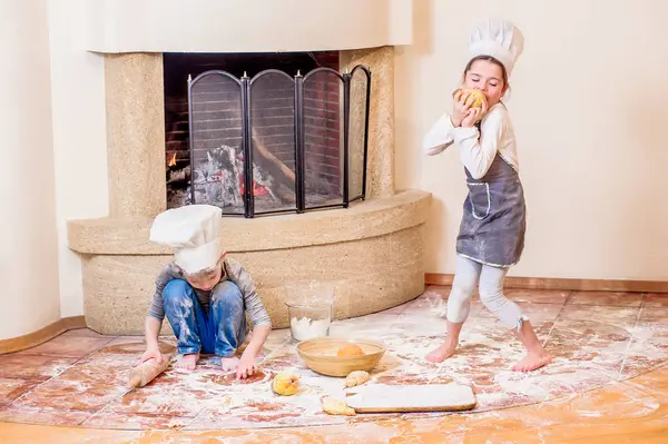 İki kardeş, erkek ve kız, şöminenin yanında şef şapkası takıyorlar. 
