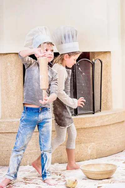 İki kardeş, erkek ve kız, şöminenin yanında şef şapkası takıyorlar. 