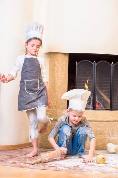 İki kardeş, erkek ve kız, şöminenin yanında şef şapkası takıyorlar. 