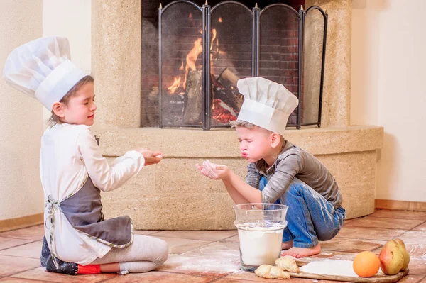 İki kardeş, erkek ve kız, şöminenin yanında şef şapkası takıyorlar. 
