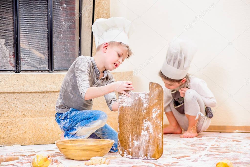Two siblings - boy and girl - in chef's hats near the fireplace 