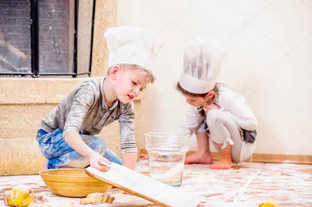 Two siblings - boy and girl - in chef's hats near the fireplace 