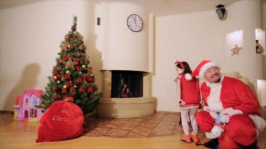 İyi yeni yıl ruhu: Noel ağacı, Hediyelik çanta, şömine - baba, kızı ve büyük oğlu aptalı oynuyor. Bir adam bir şişme oyuncak kız elf küçük boynuzları ile atlama Noel Baba kılığında. Genç onları takip ediyor