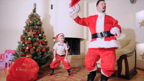 gute Neujahrsstimmung: Weihnachtsbaum, Geschenktüte, Kamin - Männer und Jungen krabbeln, spielen den Narren. Mann als Weihnachtsmann gekleidet, blauäugiger Junge mit Fliege, Weihnachtsmann roter Mütze, roter Hose und hohen Socken springt, er ist Elfe
