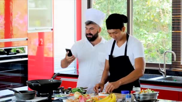 職場の同僚 タイ料理を作るキッチンでタイ料理とヨーロッパのシェフ 電話で Selfies を取って 楽しんで 経験を共有 — ストック動画