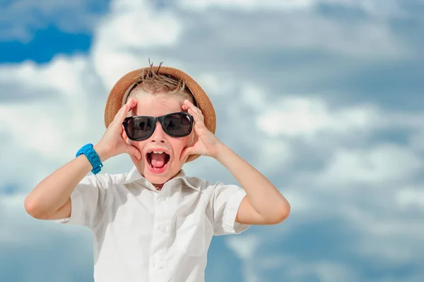 Blisko do portretu na tle chmur: przystojny mały chłopiec ubrany w slim fit koszula z okulary przeciwsłoneczne i kapelusz fedora, on podniósł ręce na jego twarz i krzyczy w — Zdjęcie stockowe