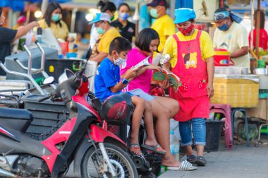 Koh Samui, Tayland - 30 Mart 2020: COVID-19 ile ilişkili tehlikelere rağmen sokak satıcıları çalışmaya devam ediyor. Çocuklar aileleriyle kalıp kitaplarla kendilerini eğlendirirler.