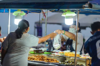 Koh Samui, Tayland - 30 Mart 2020: Covid-19 ile ilişkili tehlikelere rağmen sokak satıcıları çalışmaya devam ediyor. Önlemler alınıyor: satıcıların ve müşterilerinin maskeleri, raflarda el dezenfektanı.