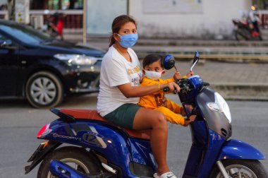 Koh Samui, Tayland - 30 Mart 2020: Küçük çocuk ve annesi motosikletle yerel bir markete yiyecek almaya geldiler. Her ikisi de Coronavirus COVID-19 'un yayılmasını önlemek için maske takıyor..
