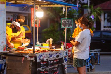 Koh Samui, Tayland - 30 Mart 2020: sokak satıcıları çalışmaya devam ediyor, küçük çocuk ailesiyle yiyecek almaya geliyor. Önlemler alındı: el dezenfektanı, satıcıların maskeleri ve onların küçük müşterileri ve anneleri..