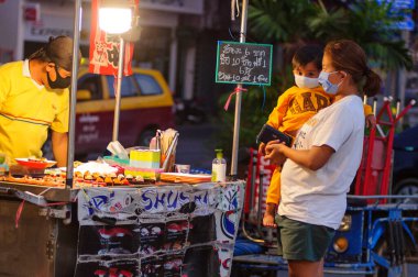 Koh Samui, Tayland - 30 Mart 2020: sokak satıcıları çalışmaya devam ediyor, küçük çocuk ailesiyle yiyecek almaya geliyor. Önlemler alındı: el dezenfektanı, satıcıların maskeleri ve onların küçük müşterileri ve anneleri..