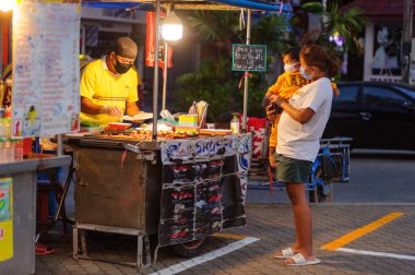Koh Samui, Tayland - 30 Mart 2020: sokak satıcıları çalışmaya devam ediyor, küçük çocuk ailesiyle yiyecek almaya geliyor. Önlemler alındı: el dezenfektanı, satıcıların maskeleri ve onların küçük müşterileri ve anneleri..