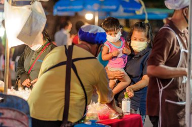 Koh Samui, Tayland - 30 Mart 2020: sokak satıcıları çalışmaya devam ediyor, küçük çocuk ailesiyle yiyecek almaya geliyor. Önlemler alındı: el dezenfektanı, satıcıların maskeleri ve onların küçük müşterileri ve anneleri..