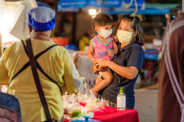 Koh Samui, Tayland - 30 Mart 2020: sokak satıcıları çalışmaya devam ediyor, küçük çocuk ailesiyle yiyecek almaya geliyor. Önlemler alındı: el dezenfektanı, satıcıların maskeleri ve onların küçük müşterileri ve anneleri..