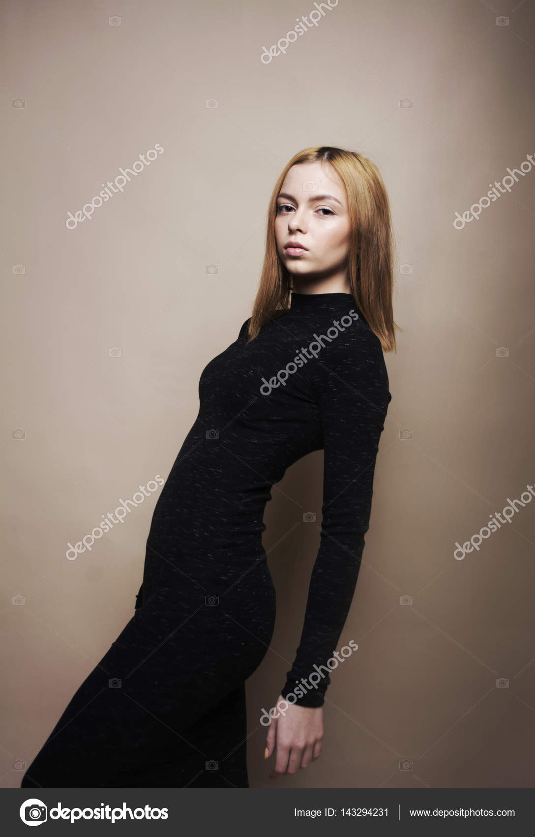 Sad girl on a beige background in a black dress. Blond girl with
