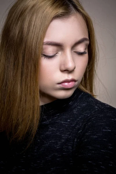 Ragazza triste su uno sfondo beige, in un abito nero. Ragazza bionda con i capelli corti guardando nella fotocamera, trucco delicato. Una ragazza snella in un vestito con le maniche lunghe. Sta lateralmente e si appoggia all'indietro . — Foto Stock