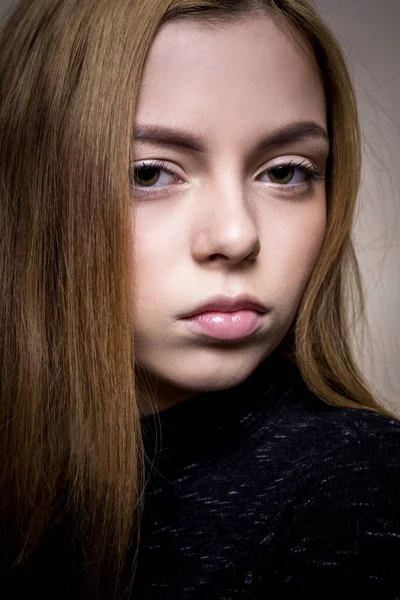 Ragazza triste su uno sfondo beige, in un abito nero. Ragazza bionda con i capelli corti guardando nella fotocamera, trucco delicato. Una ragazza snella in un vestito con le maniche lunghe. Sta lateralmente e si appoggia all'indietro . — Foto Stock