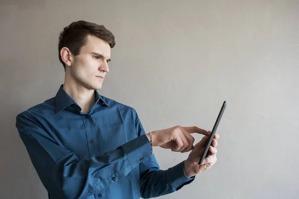 Uzak tablet vasıl seyir yakışıklı bir adam portresi. Bir yeşil gömlek. Esmer yeşil gözlü. Bir tek sesli gri arka plan üzerinde. Hafifçe gülümsüyor. Adam rüya. Mutlu genç adam gri arka plan üzerinde izole dijital Tablet kullanma