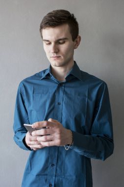 Telefonun yan seyir yakışıklı bir adam portresi. Mor bir gömlek. Esmer yeşil gözlü. Bir tek sesli gri arka plan üzerinde. Hafifçe gülümsüyor. Adam rüya. Mutlu genç adam kullanarak dijital telefon izole gri arka plan