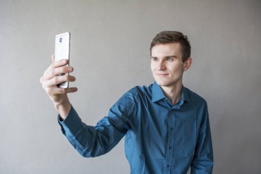 Elinde telefonla kameraya bakarak yakışıklı bir adam portresi. Adam kendini fotoğraf yapar. Mor bir gömlek. Esmer yeşil gözlü. Bir tek sesli gri arka plan üzerinde. Adam hayal.