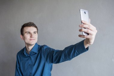 Elinde telefonla kameraya bakarak yakışıklı bir adam portresi. Adam kendini fotoğraf yapar. Mor bir gömlek. Esmer yeşil gözlü. Bir tek sesli gri arka plan üzerinde. Adam hayal.
