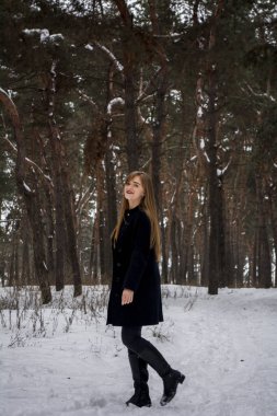 Karlı bir ormandaki güzel kız. Uzun saçlı sarışın. Gülümseyen