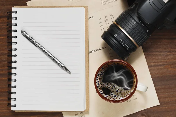 Καφέ στο φλιτζάνι, σημειωματάριο και μια φωτογραφική μηχανή Dslr στο τραπέζι — Φωτογραφία Αρχείου