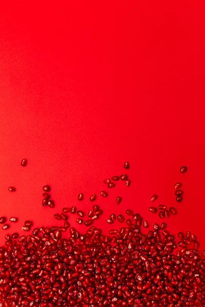 Pomegranate seeds on a red background. Vertical orientation. The view from the top.The scattered red grains of a pomegranate. Garnet on the border of the image with copy space for text.